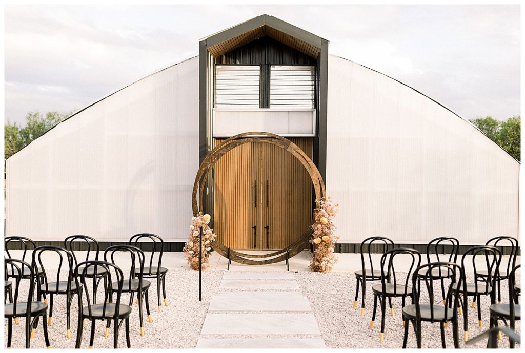 wedding ceremony in front of greenhouse venue with circle arch