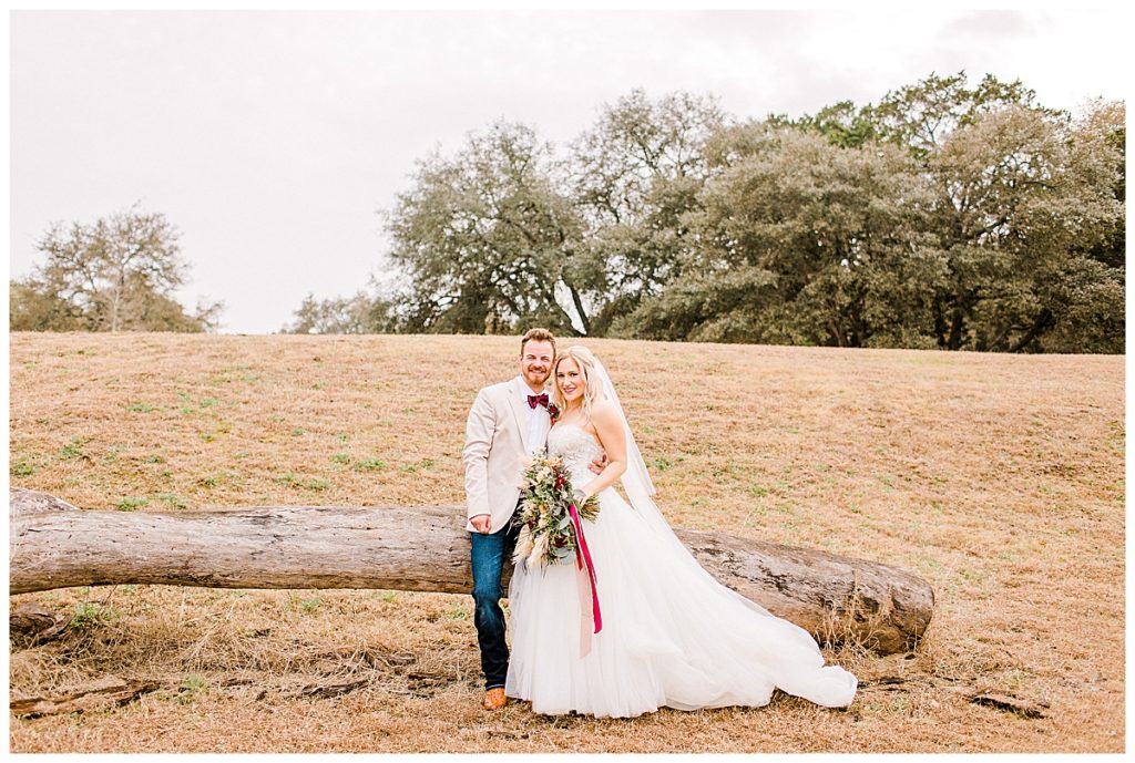 bride and groom sitting on tree limb in field