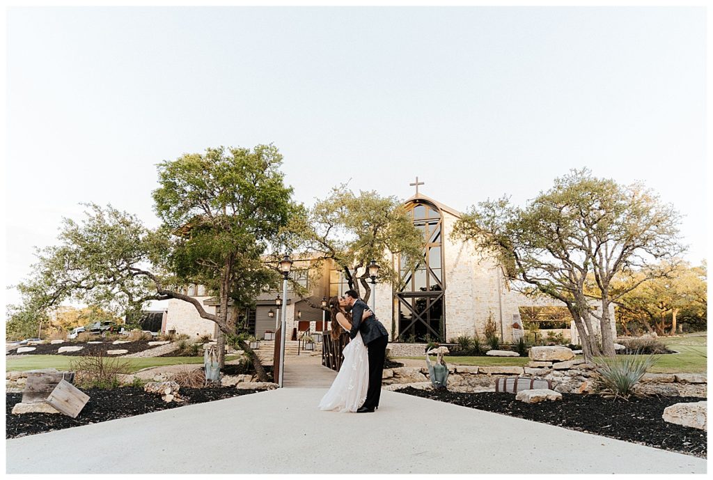 groom dips and kisses bride in front of venue